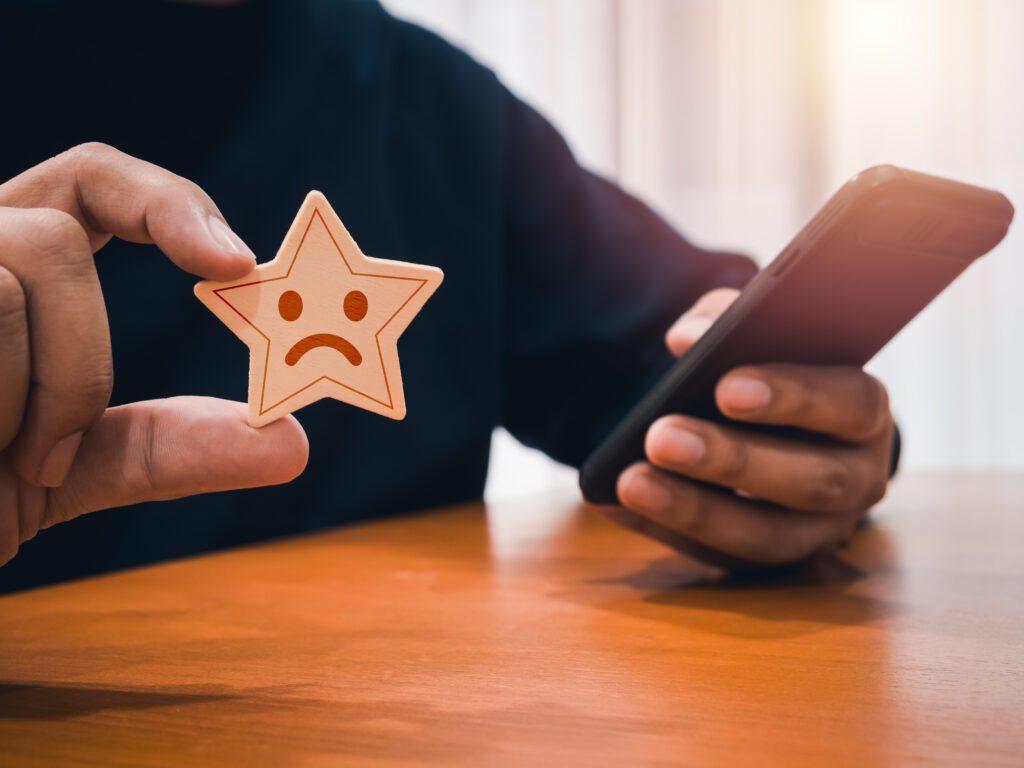wooden star with sad face emotion holding by mans hand who using smartphone service rating app customer evaluation ratings feedback client experience satisfaction survey concepts